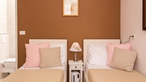 Une chambre à coucher avec deux lits, chacun doté d’une tête de lit blanche, de coussins roses et beiges, et d’une petite table de chevet avec une lampe.