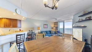 A spacious living area with a wooden dining table, blue sofa, and a view of the ocean through large windows. - Southpoint 707 La Casa Azul (Ponce Inlet)