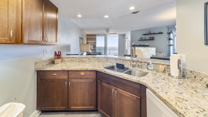 A kitchen with granite countertops, wooden cabinets, a stainless steel sink, and a view to the outside. - Southpoint 707 La Casa Azul (Ponce Inlet)