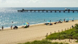 Una spiaggia con un molo che si protende nell'acqua, persone che si rilassano sulla sabbia e ombrelloni che offrono ombra.