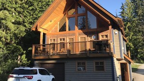 A two-story log cabin with a balcony, a garage, and a white SUV parked in front. - Unbeatable Chalet at Base of Red Mountain (Rossland)