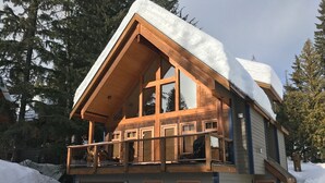A two-story log cabin with a balcony, surrounded by snow and trees. - Unbeatable Chalet at Base of Red Mountain (Rossland)