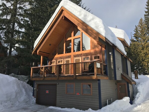 A two-story log cabin with a balcony, surrounded by snow and trees. - Unbeatable Chalet at Base of Red Mountain (Rossland)