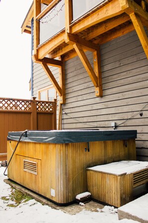 A wooden hot tub with a metal frame, positioned against a house with a wooden deck and a lattice fence. - Unbeatable Chalet at Base of Red Mountain (Rossland)