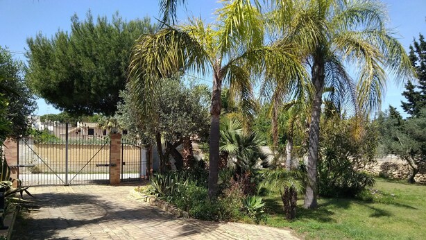 A paved pathway leading to a gated entrance surrounded by lush greenery and palm trees. - Depandance Venera in Marsala with free wifi and air condition (Marsala)