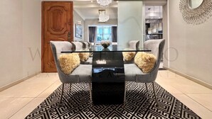 A modern dining area with a glass table, grey upholstered chairs with fluffy cushions, a patterned rug, and a chandelier. - Come relax and enjoy Rio in Modern Ipanema Luxury! (Rio de Janeiro)