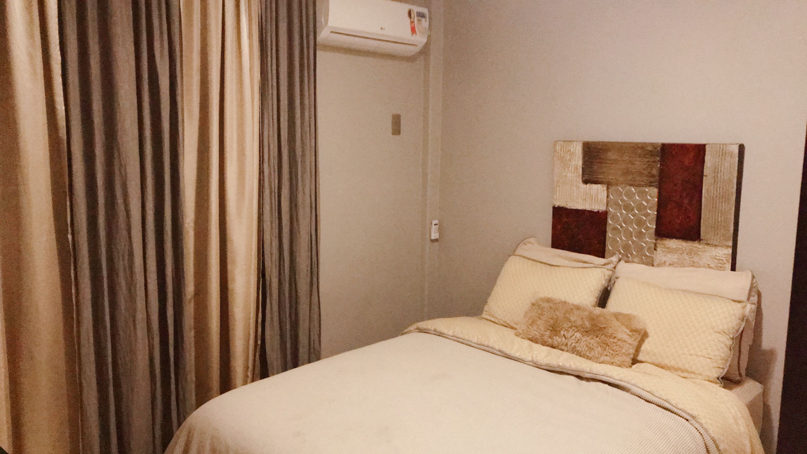 Una camera da letto con un letto, tende, un condizionatore d'aria a parete e una testiera con motivo geometrico.
