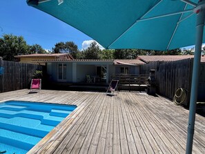 Um quintal com piscina, deck de madeira e área de varanda coberta.