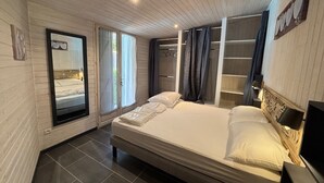 A bedroom with a bed, a wardrobe, a mirror, and a window. - Near SOULAC/mer, air-conditioned house with heated indoor pool sleeps 4 (Grayan-et-l'Hôpital)
