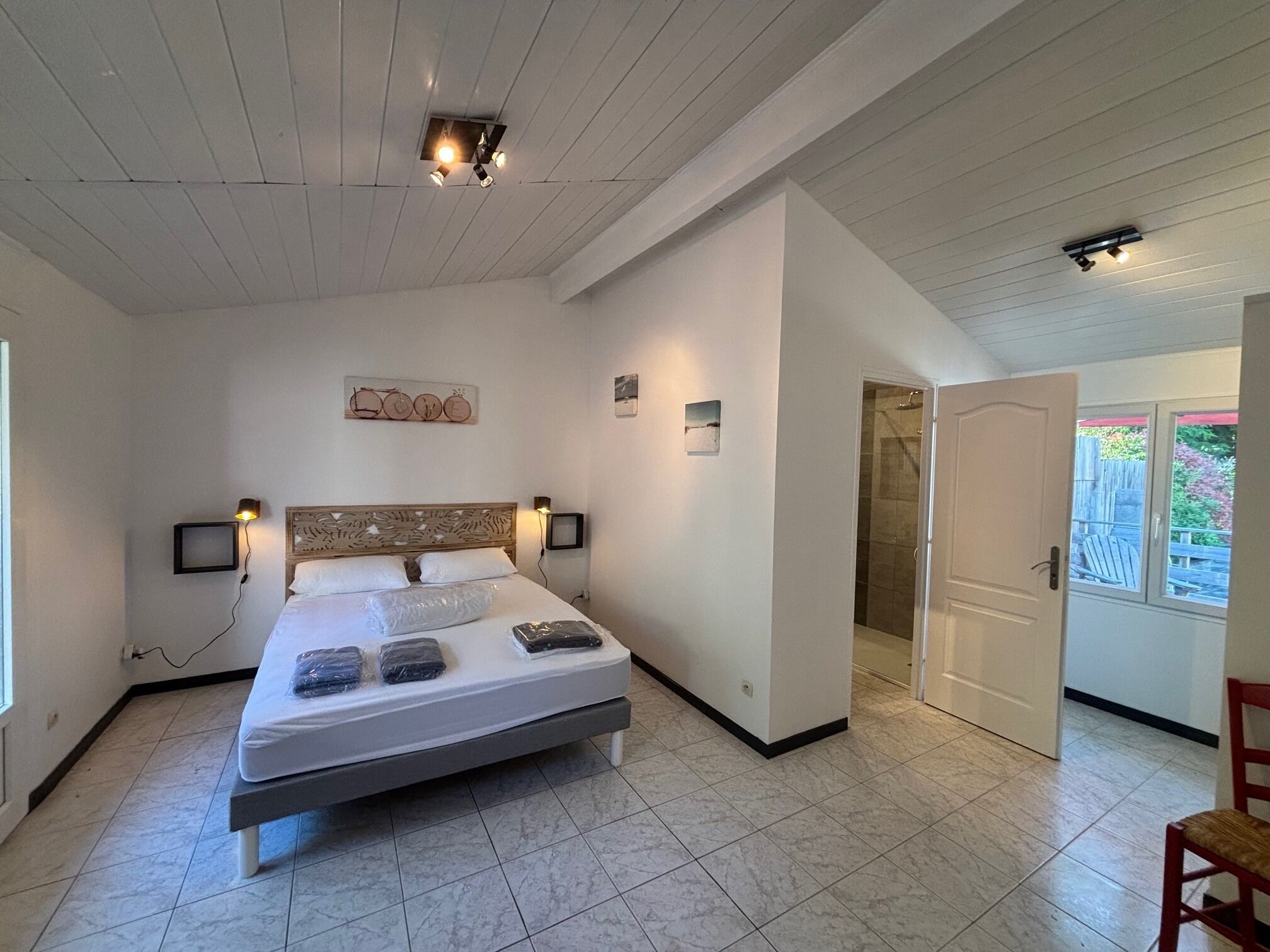 Een slaapkamer met een bed, nachtlampjes, een houten hoofdbord, een kleine televisie en een deur naar een badkamer.