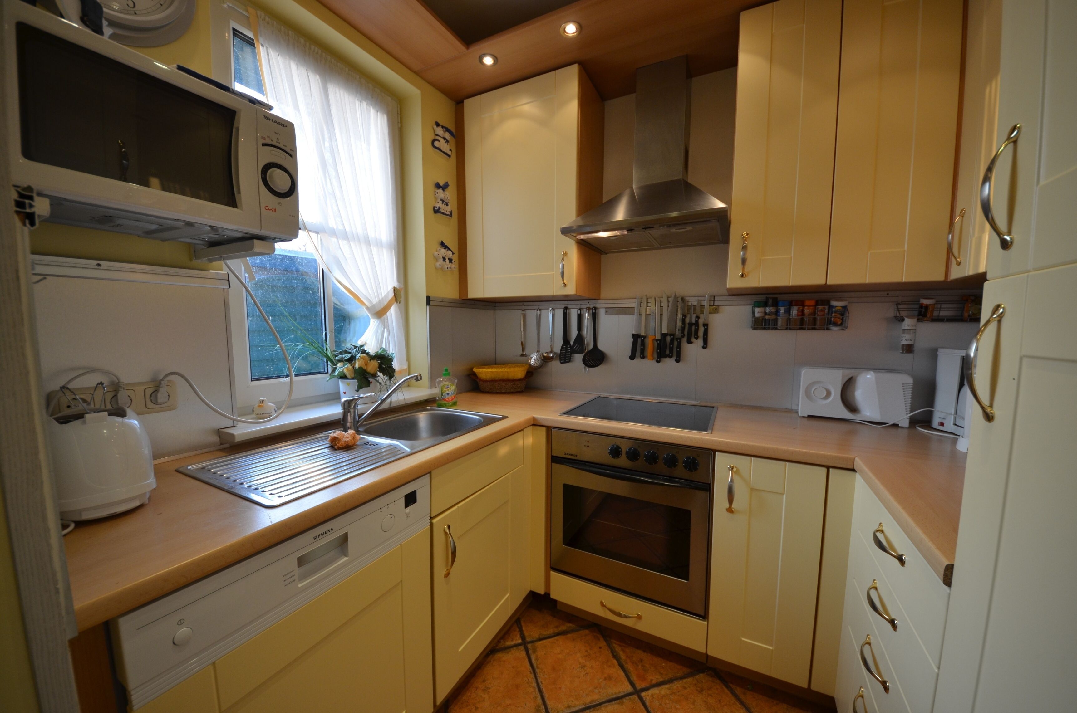 A compact kitchen with a microwave, oven, sink, and various utensils.
