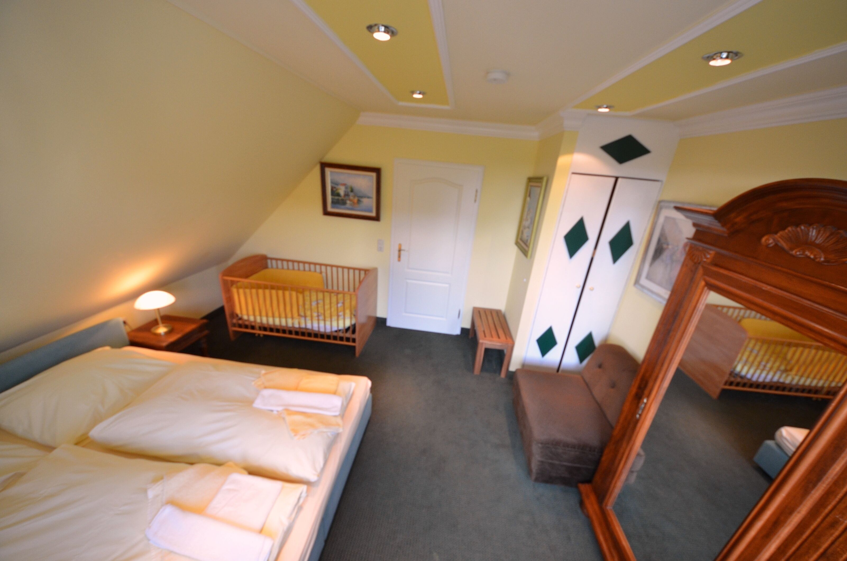 A room with a bed, a crib, a wooden cabinet, and a door.