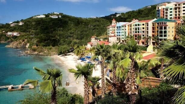 A coastal hotel with multiple colorful buildings, a beach, and palm trees.