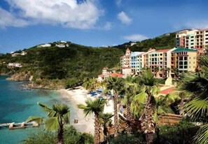 A coastal hotel with multiple colorful buildings, a beach, and palm trees.