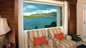 A room with a large window offering a view of a coastal landscape with boats.