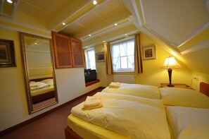 Een hotelkamer met twee bedden, een grote spiegel, een raam met gordijnen, een lamp en een radiator.
