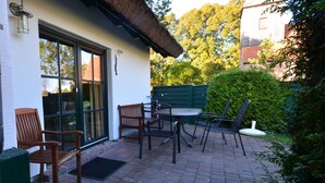 Une terrasse extérieure avec une table et des chaises, un banc en bois et une clôture verte.