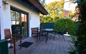 Een terras buiten met een tafel en stoelen, een houten bank en een groene hek.