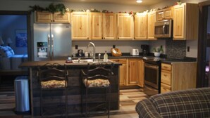 A modern kitchen with wooden cabinets, a stainless steel refrigerator, a microwave, and a built-in oven. There is a bar area with stools and a sink. - Elk Haven Vacation Cabins, Custer SD, Elk Haven Vacation Cabins, Custer SD (Custer)