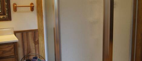 A bathroom with a shower, wooden floor, a towel rack, and a wicker basket.