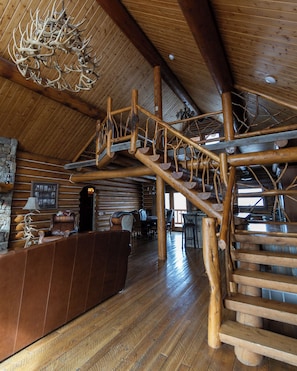 A rustic interior with a wooden staircase, a reception desk, and a chandelier.