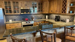 A kitchen with wooden cabinets, a stove, a microwave, and a bar area with wooden chairs. - Teton Club - 3 Bedroom/3 Bath, Ski in/Ski out, 2 free lift tickets (Teton Village)