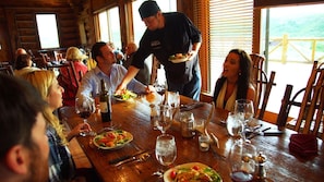 A wooden dining table with plates of food, wine glasses, and a bottle of wine. - Cozy Two Bedroom Cabin on Private Montana Dude Ranch - Angler's Perch (Belt)