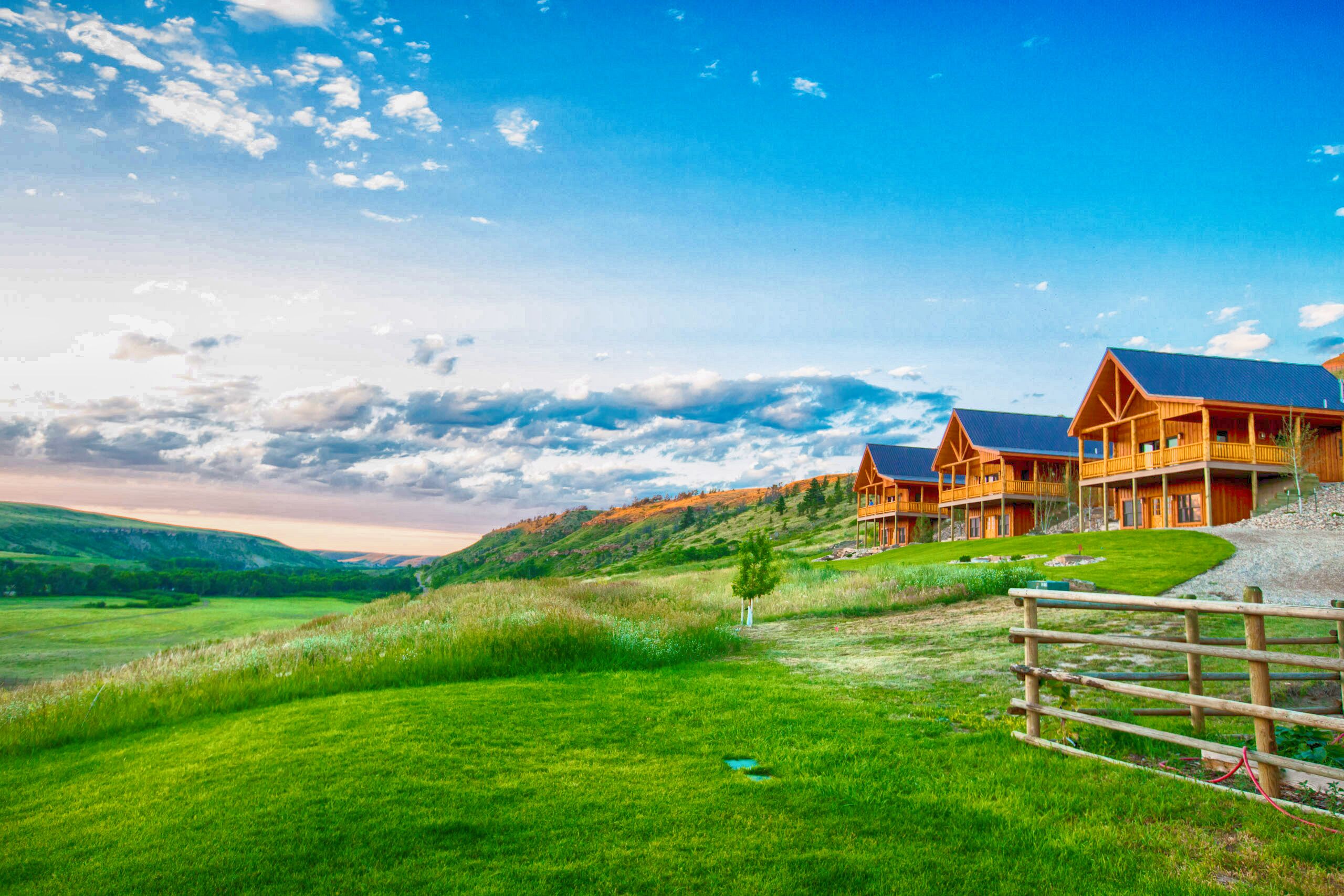 A lodge with multiple wooden cabins, a grassy field, and a hilly landscape.