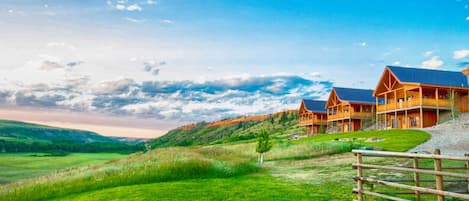 A lodge with multiple wooden cabins, a grassy field, and a hilly landscape.