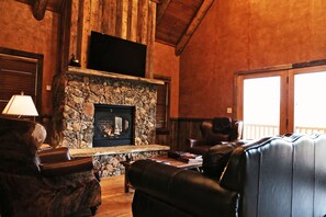 A cozy living room with a stone fireplace, leather sofas, and a flat-screen TV mounted above the fireplace. - Cozy Two Bedroom Cabin on Private Montana Dude Ranch - Angler's Perch (Belt)