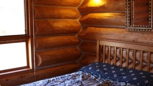 A log cabin room with a wooden bed, a window, and a wall-mounted light fixture. - Log Chalet with Mountain views and private lake (Lumby)