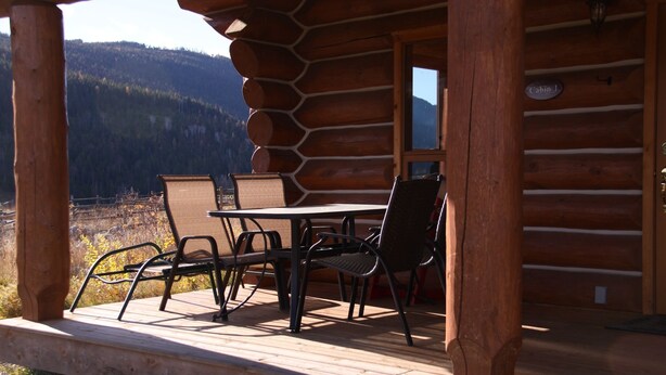 A wooden cabin with a dining area featuring a table and chairs, a window, and a sign reading "Cabin 1". - Log Chalet with Mountain views and private lake (Lumby)