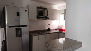 A compact kitchen with a stainless steel refrigerator, a microwave, a gas stove, and a blender. - APARTMENT IN NORTH PRADOS (Cali)