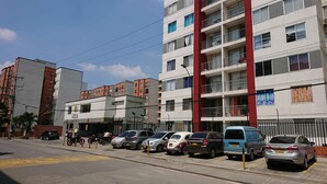 A multi-story building with a commercial ground floor, several parked cars, and a clear sky. - APARTMENT IN NORTH PRADOS (Cali)