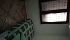 Ein Zimmer mit Fliesenboden, einem Fenster mit gemusterten Jalousien und einem grün-weißen Möbel.