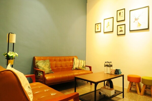 A living room with a brown leather sofa, a coffee table, and a small table with water bottles and cups. There are framed pictures on the wall. - Lu-Kang Traveler Inns (Lukang)