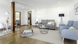 A modern living room with a gray sofa, a blue armchair, a glass coffee table, and a dining area with a white table and chairs. - Always Easy I Ático Plaza (San Sebastián/Donostia)