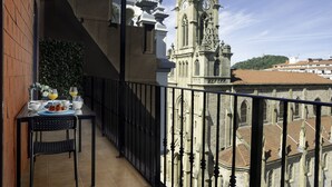 A balcony with a table set for breakfast, a wrought iron railing, and a view of a historic building with a clock tower. - Always Easy I Ático Plaza (San Sebastián/Donostia)
