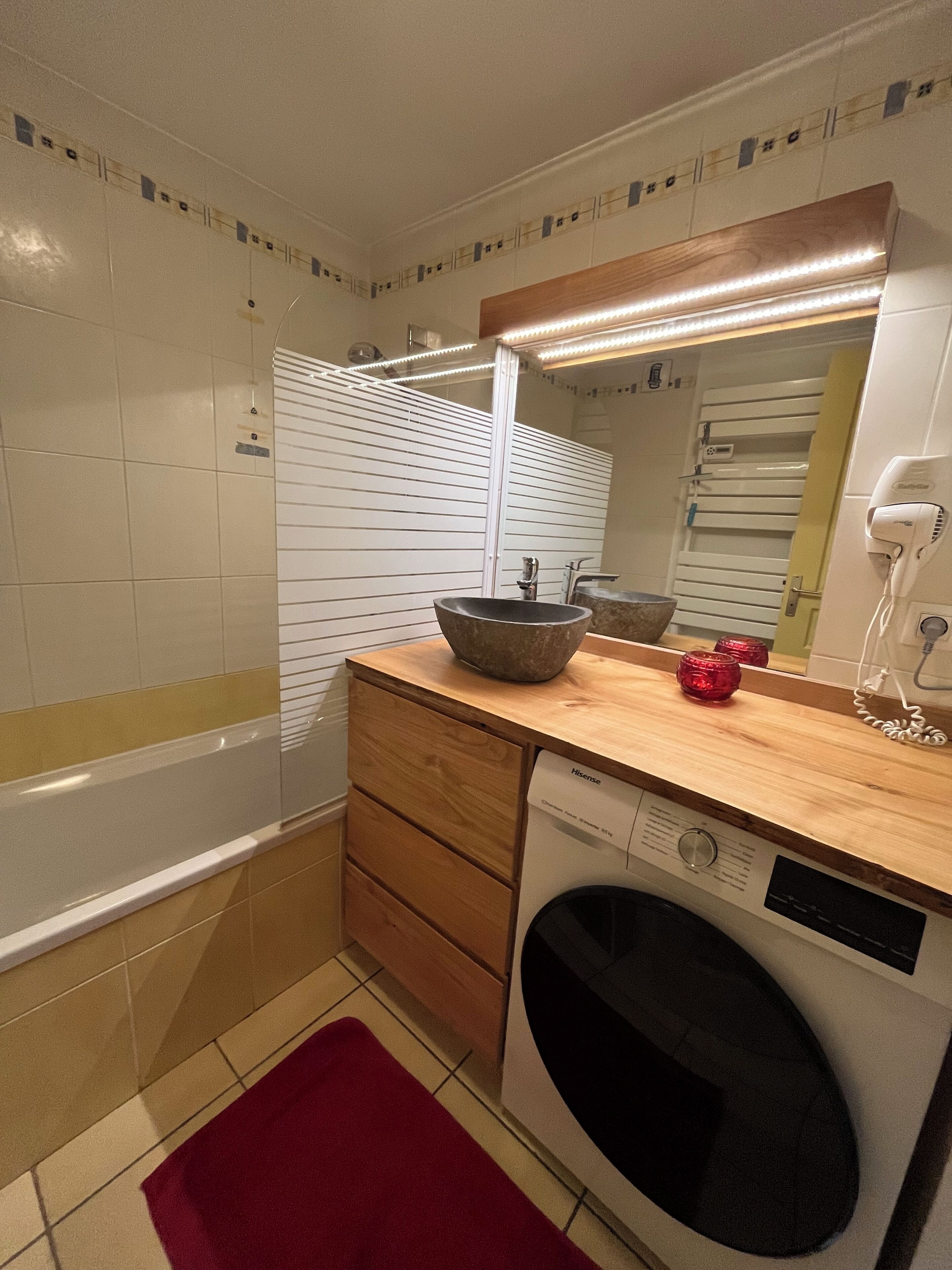 Ein Badezimmer mit einem Holzausziehtisch, einem Waschbecken mit Natursteinbecken, einem Spiegel, einem Fön und einer Waschmaschine.
