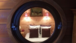 A circular wooden window with a bed and two wall-mounted lamps.