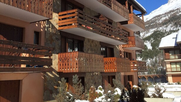 A multi-story building with wooden balconies, snow-covered roofs, and a mountainous backdrop.