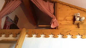 A wooden loft bed with a slanted ceiling, a teddy bear, and checkered curtains.