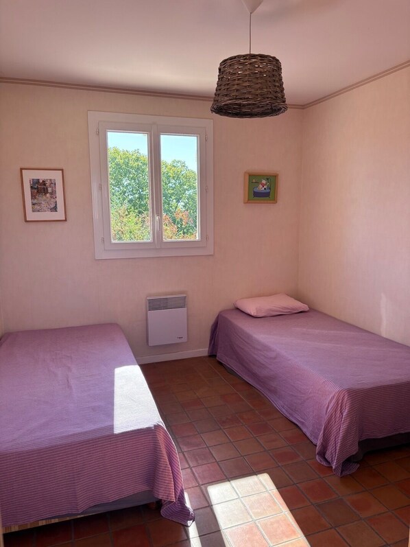 Una habitación con dos camas, una ventana con vistas a árboles, un calentador de pared y una lámpara colgante.