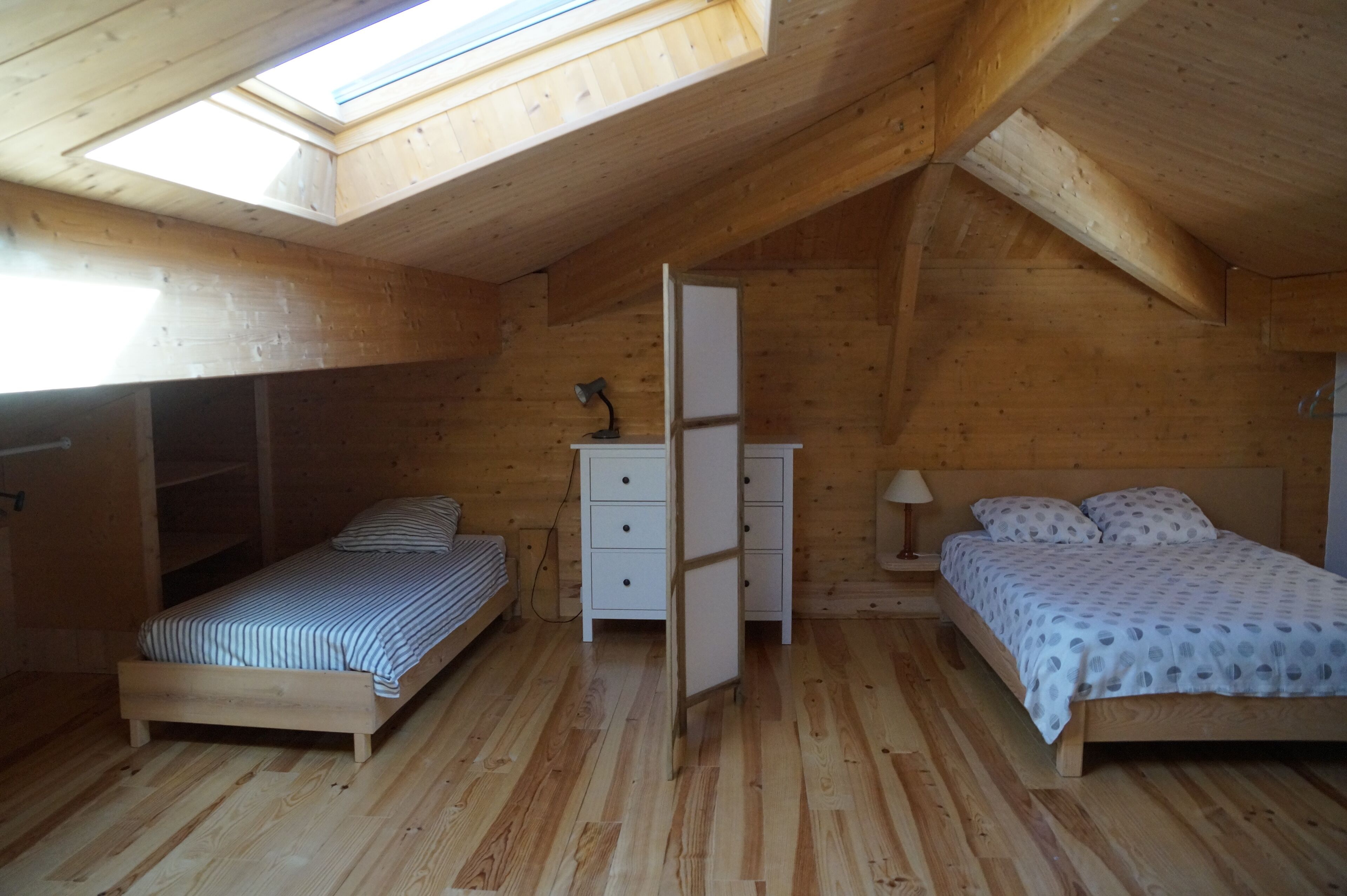 Een slaapkamer in een houten blokhut met twee bedden, een witte dressoir en een dakraam.