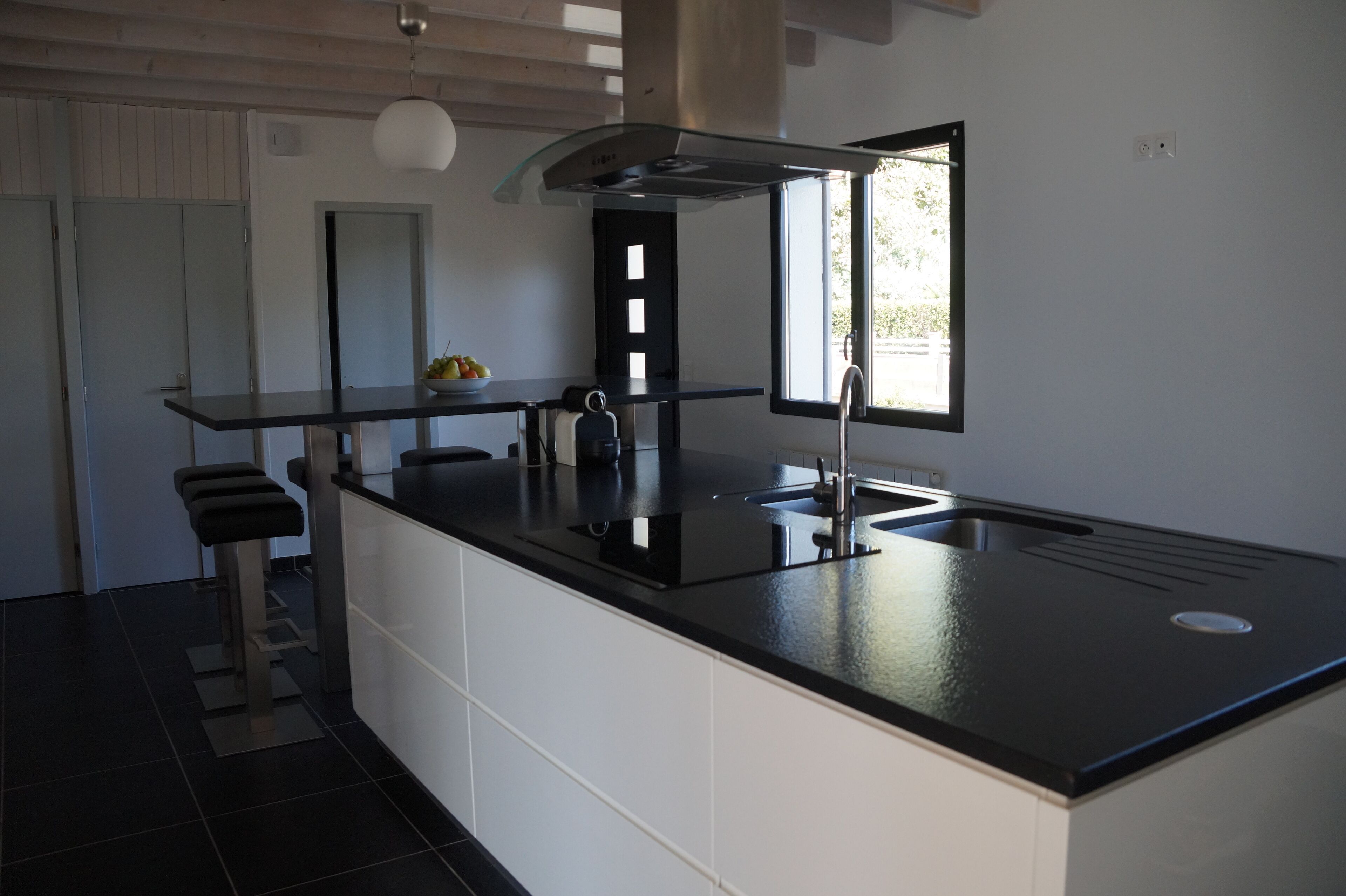 A modern kitchen with a black countertop, white cabinets, a stainless steel range hood, and a window providing natural light.