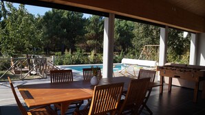 Un patio exterior con mesa y sillas de madera, una piscina y mesa de fútbol.