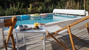 Zona de piscina con una mesa lista para una comida, un par de gafas de sol y un libro.