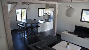 Una cocina moderna con comedor, una sala de estar con sofá y mesa de centro, y un televisor sobre un mueble blanco.