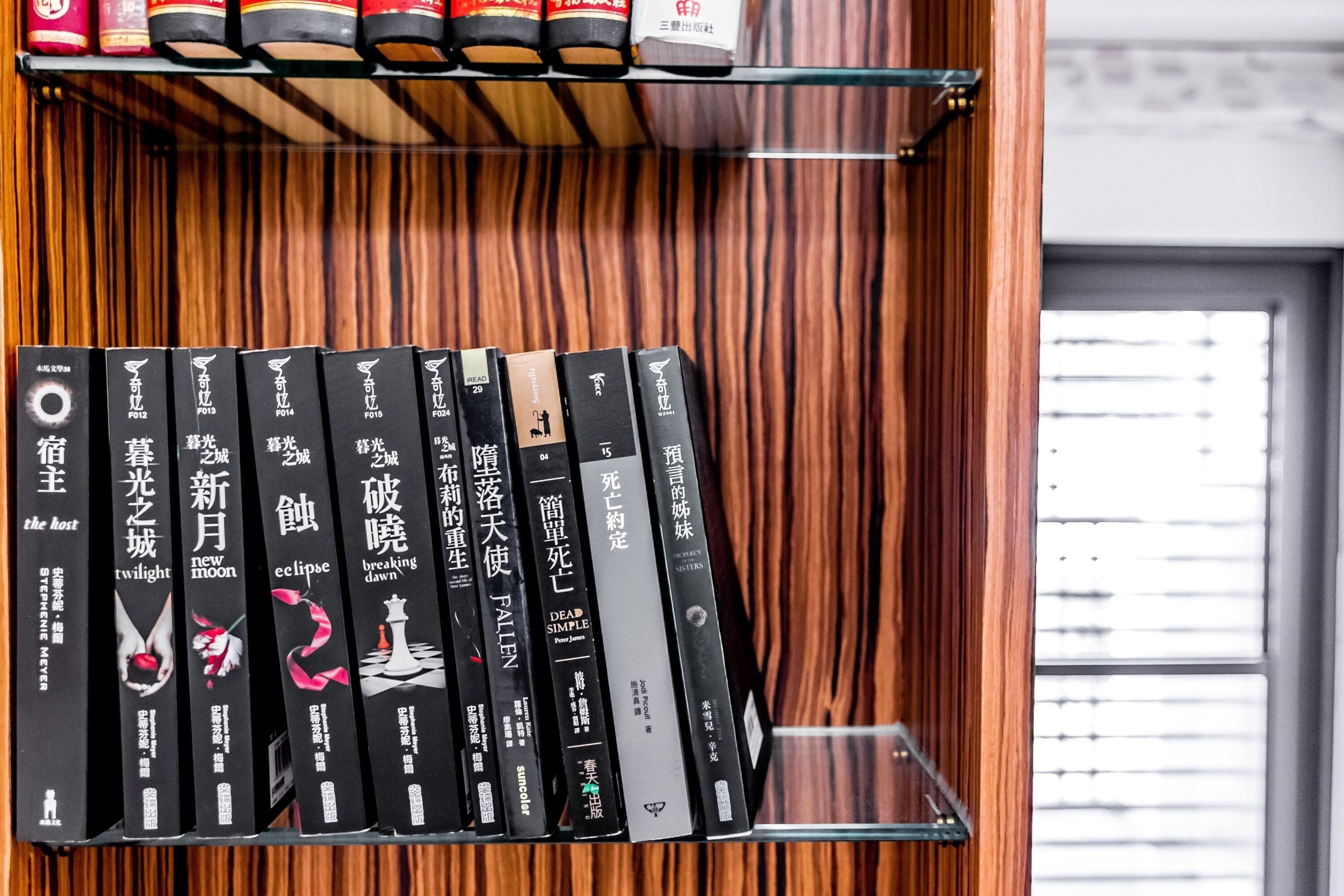 A bookshelf with a variety of books, some with foreign text, and a wooden panel wall in the background.