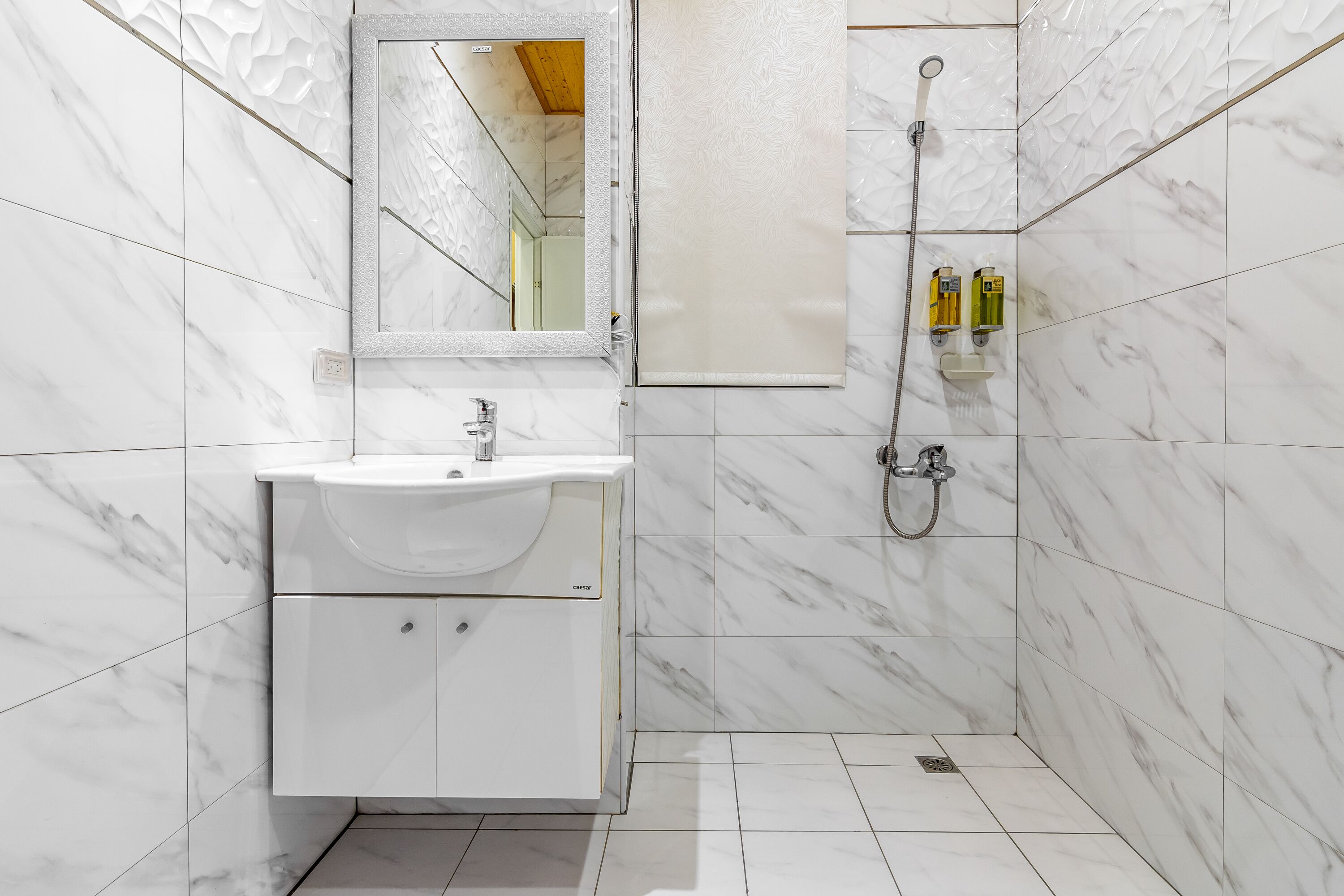Un baño con lavabo de mármol blanco, espejo y ducha.
